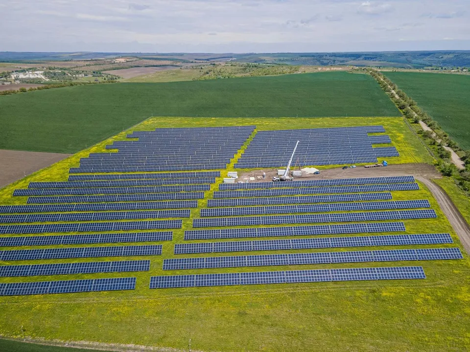 Aerial view displays a large array of solar panels being installed with crane and vehicles across rural agricultural fields on a bright day.